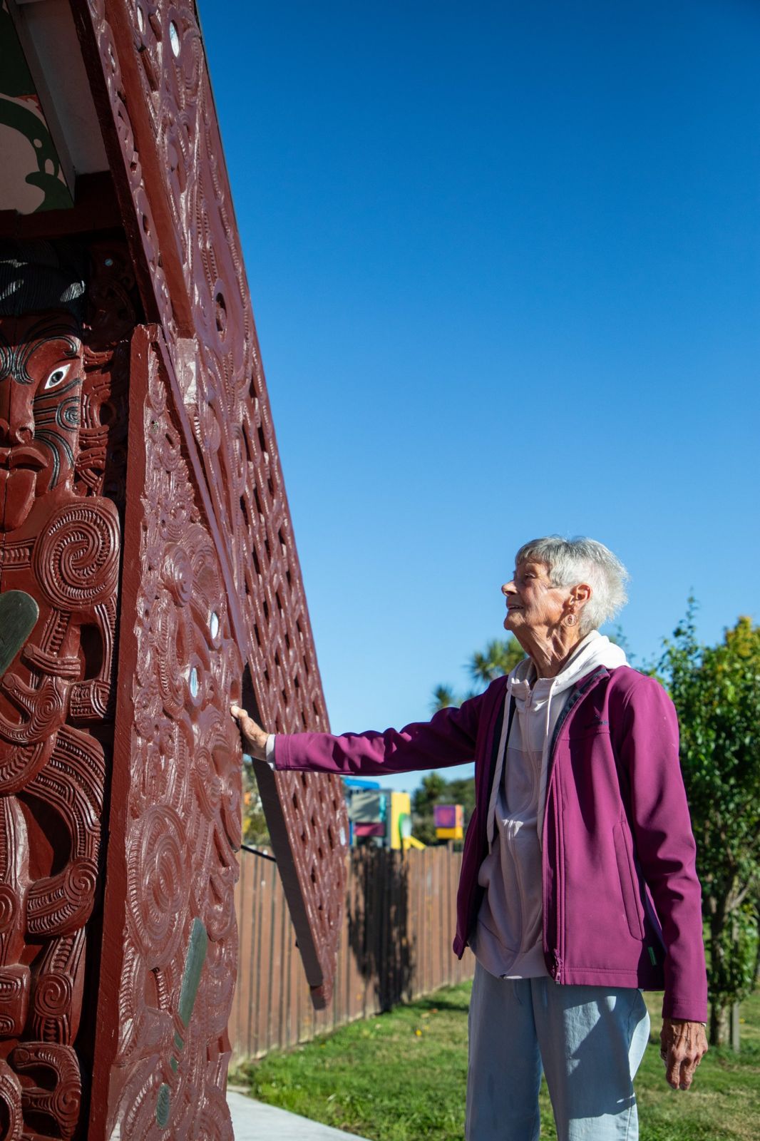 A kuia resting her hand on the carved maihi of the wharenui